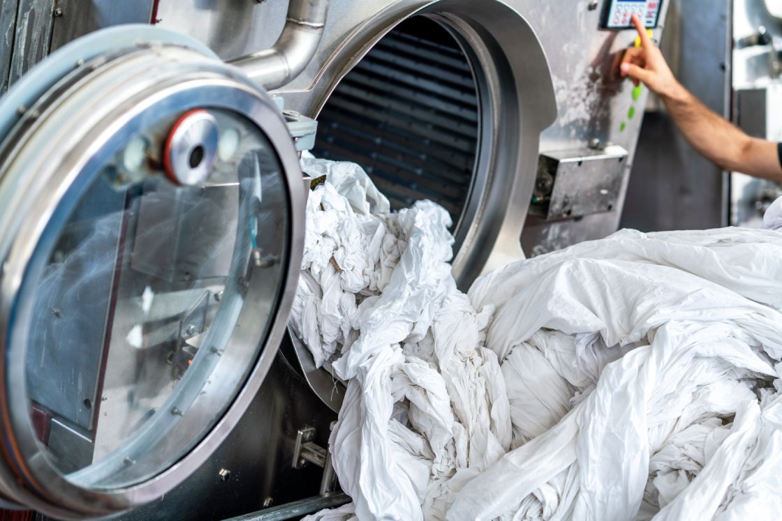 An industrial washing machine loaded with white textiles.