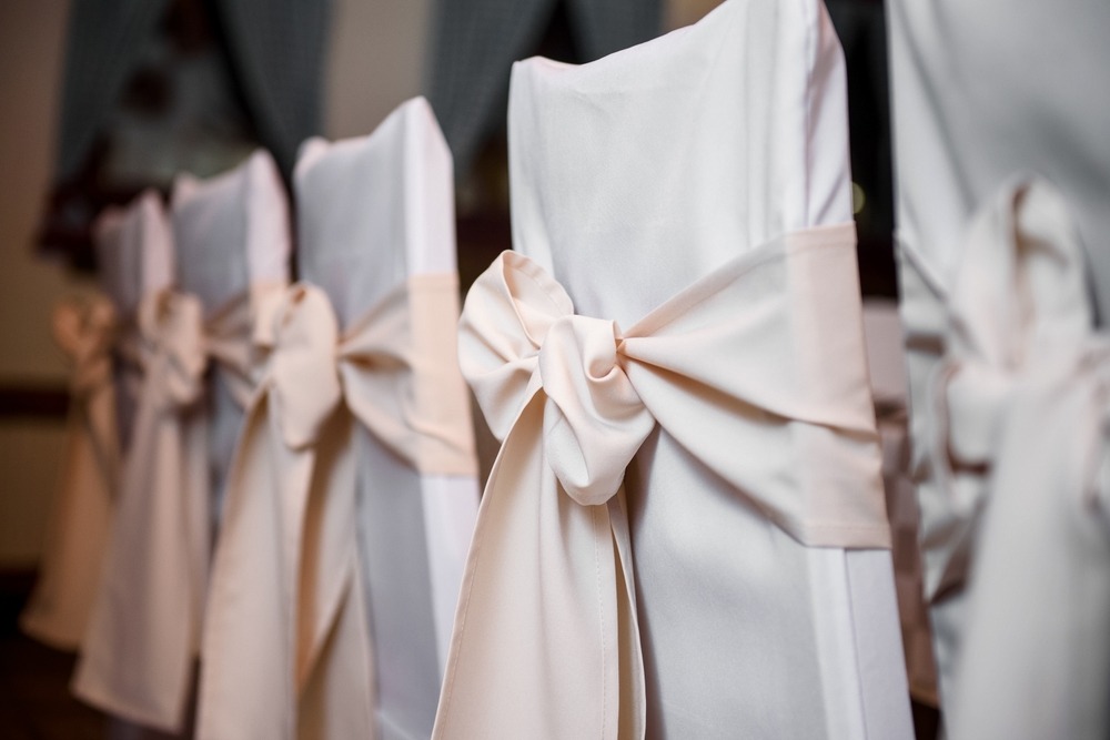 A row of banquet chairs features white chair covers and champagne-colored sashes tied into bows.