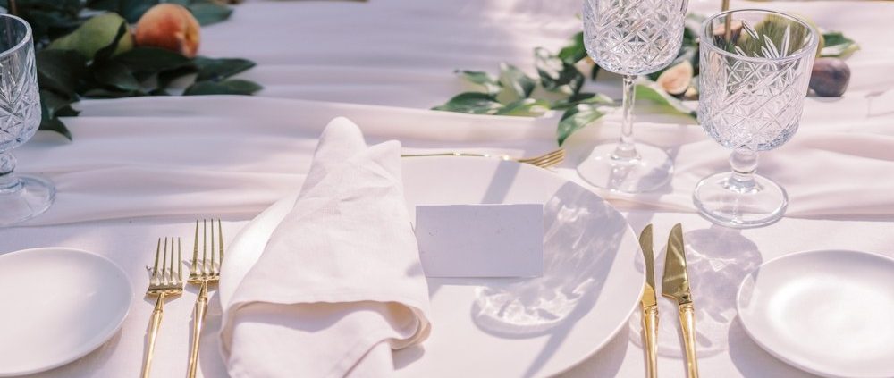 A table set with fine linens in white, featuring golden cutlery and crystal glassware.