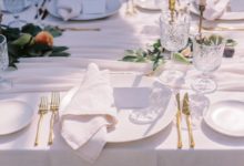A table set with fine linens in white, featuring golden cutlery and crystal glassware.