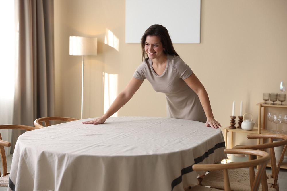 A woman lays a beige table cloth on her table at home.