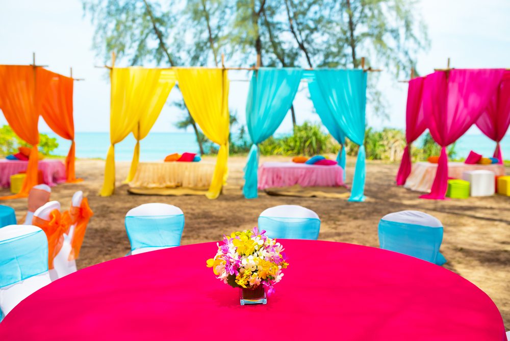 An outdoor event venue featuring colorful tablecloths, sashes, and hanging textiles.