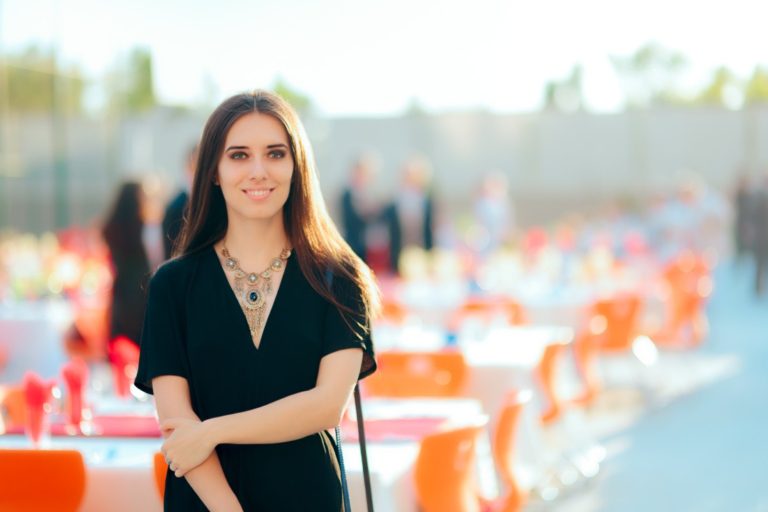 A wedding planner stands in front of her outdoor corporate event setup, complete with rented linens.